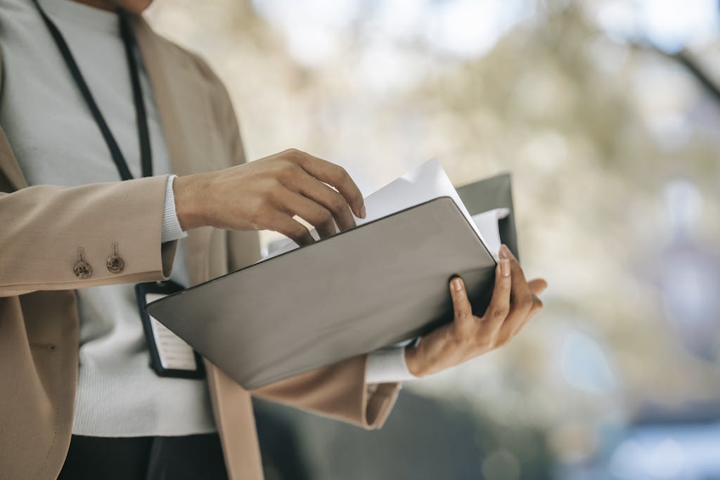 Crop anonymous female entrepreneur in elegant jacket with badge looking through papers in folder